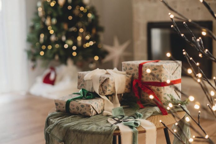 Stylish wrapped christmas gifts with ribbon on table on background of decorated christmas tree with vintage baubles, rustic fireplace and festive lights. Merry Christmas and Happy Holidays!