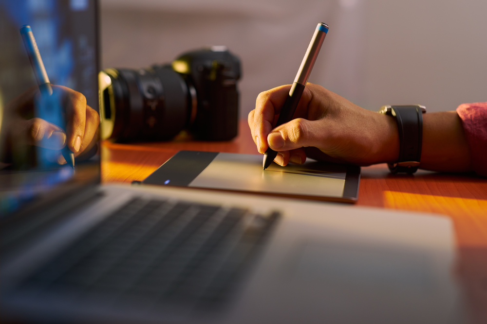Photographer drawing and retouching image on laptop computer, using a digital tablet and stylus pen
